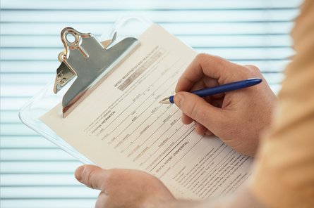 Link: Kinderwunschbehandlung und die Verbotsliste Ein Mensch füllt ein Formular auf einem Klemmbrett aus